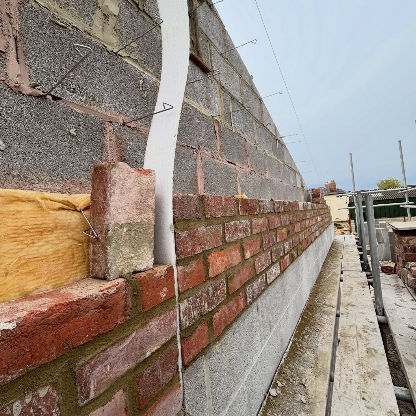 Cavity wall under construction with a concrete block inner leaf, reclaimed brick outer leaf, insulation and wall ties