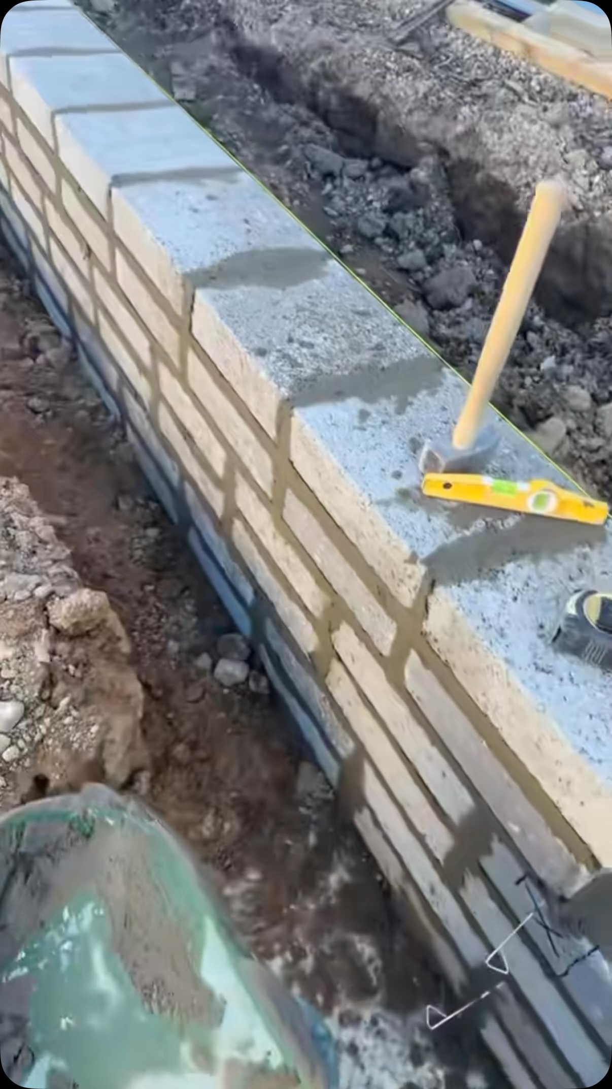 Bricklayer levelling a new block and brick wall on fresh concrete foundations with a spirit level