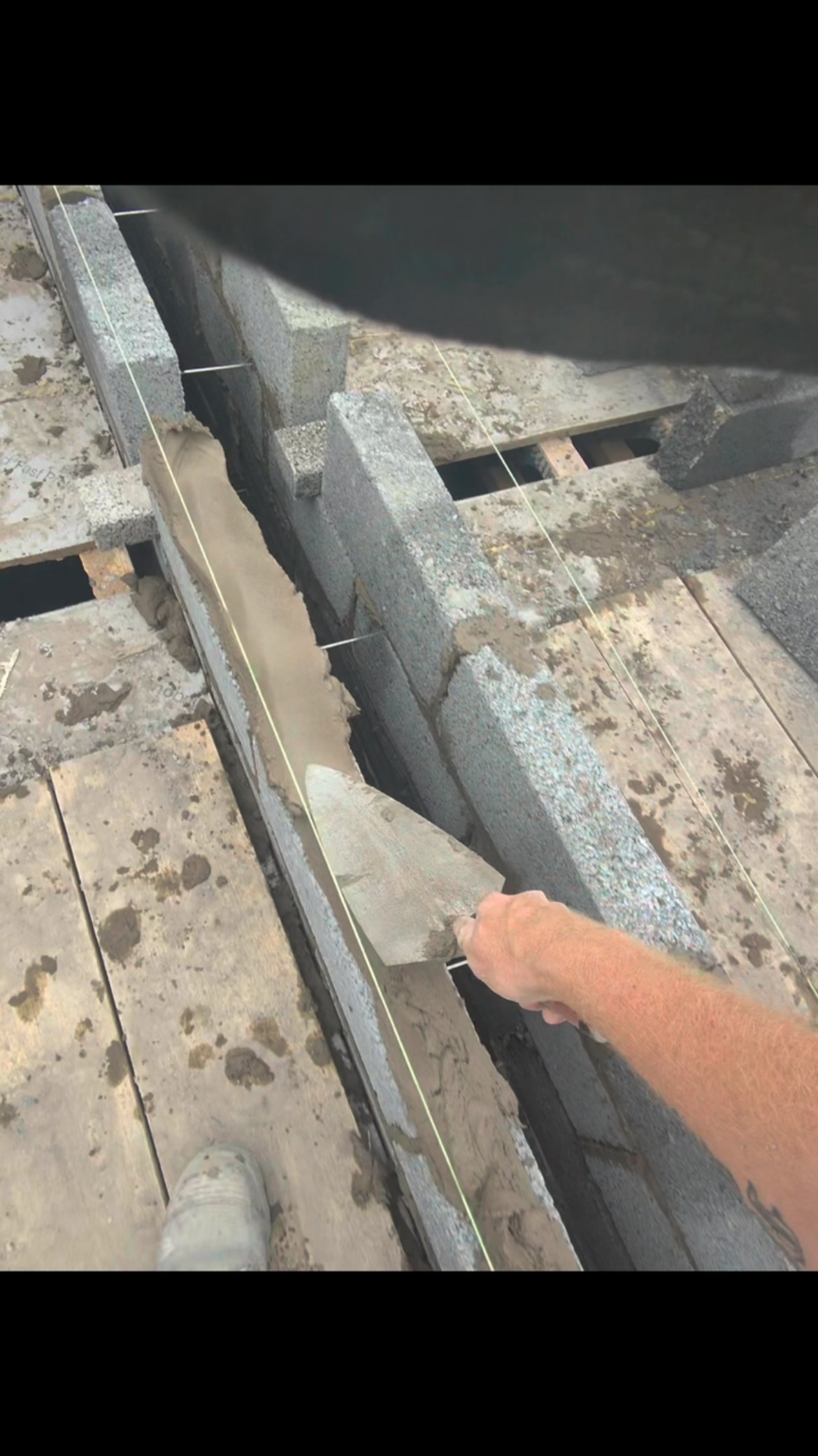 Close-up of a trowel pointing fresh mortar along a course of concrete blocks with a string line